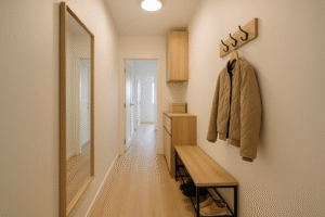 Wąski przedpokój z jasnymi ścianami, funkcjonalnymi meblami i lustrem optycznie powiększającym przestrzeń